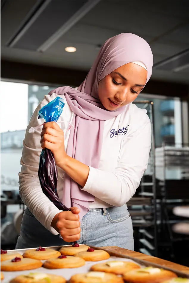 Camilla spritsar fyllning på nybakade cookies i bageriet